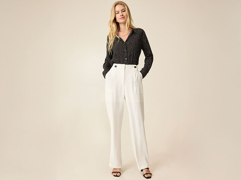 Modelo vestindo camisa e calça clara em fundo neutro
