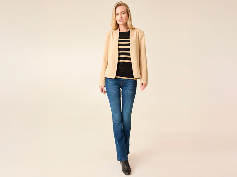 Mulher vestindo blazer bege e jeans, pose confiante.