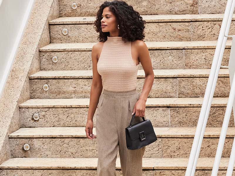 Mulher com blusa neutra e calças elegantes na escada.