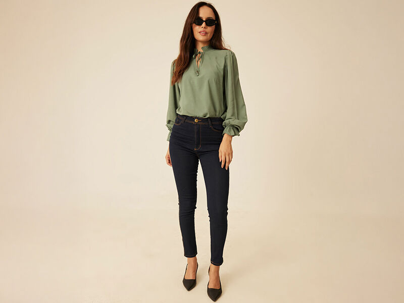 Mulher usando blusa verde e calça jeans escura.