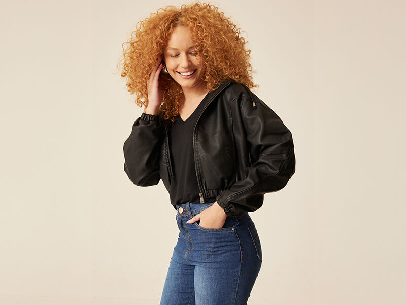 Mulher sorrindo com cabelo cacheado e jaqueta preta