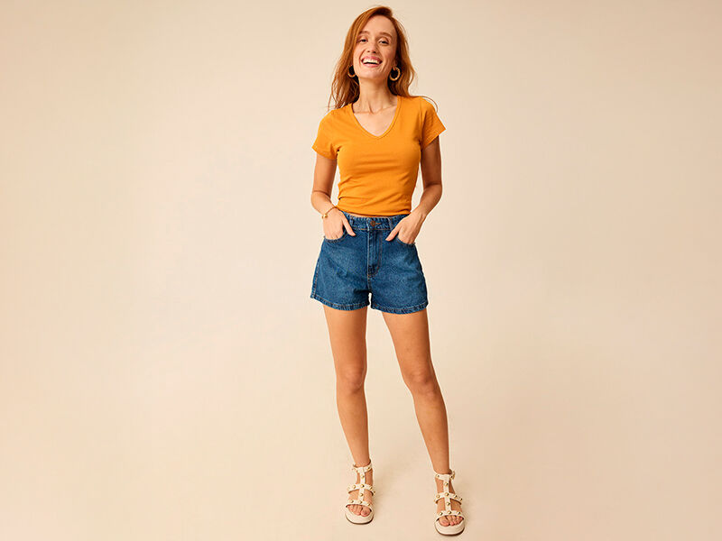Mulher sorrindo com camiseta laranja e shorts jeans