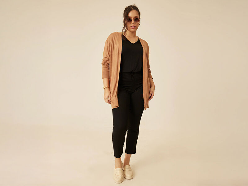Mulher usando cardigan e óculos de sol em fundo neutro