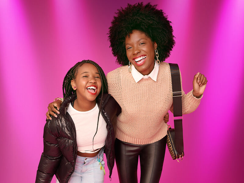 Duas mulheres sorrindo com cabelo volumoso em fundo rosa