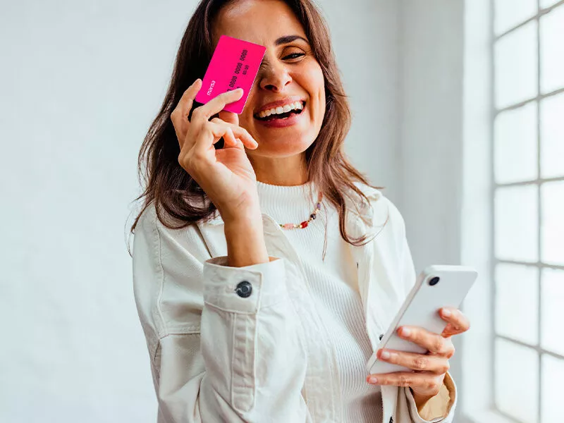 Mulher sorrindo com cartão e celular na mão.