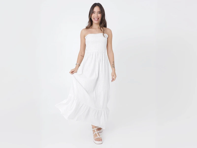 Mulher com vestido comprido branco tomara que cai e sandálias brancas de tiras. Moda feminina de verão em fundo neutro.