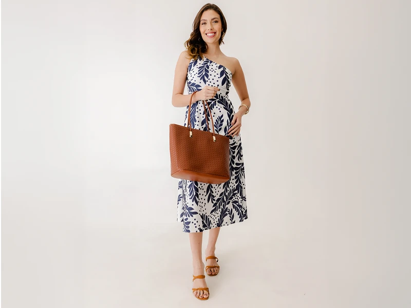 Mulher com vestido midi estampado azul e branco, mala de ombro castanha e sandálias.