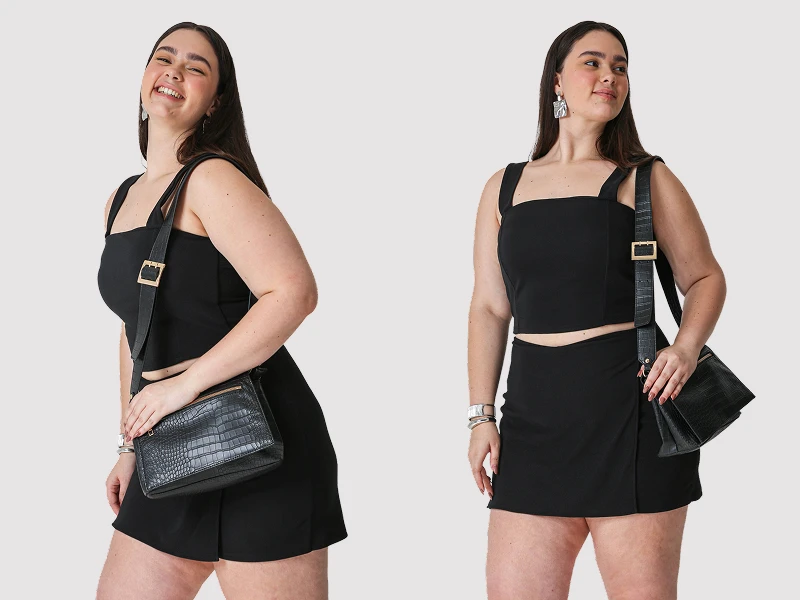 Mulher com conjunto preto de top e saia, a usar mala de ombro preta com textura de crocodilo.