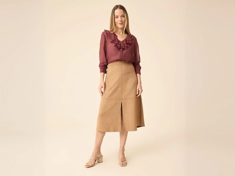 Mulher com blusa bordeaux de folhos e saia midi camel com racha central.