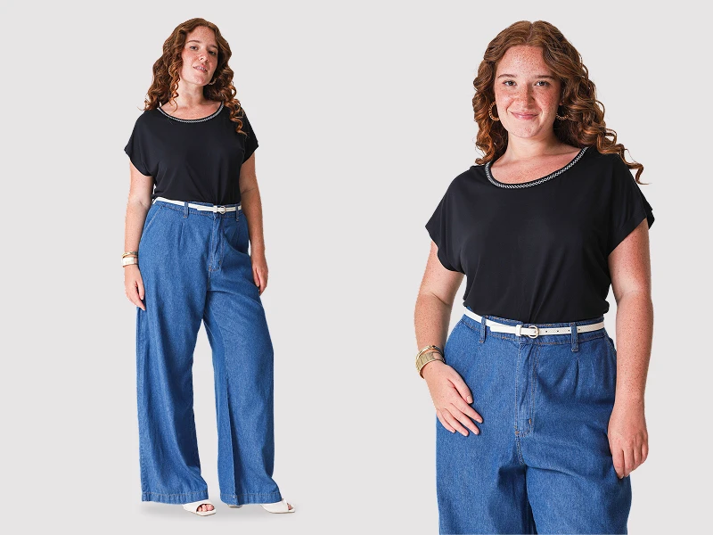 Mulher ruiva com blusa preta e calças de ganga largas com cinto branco. Look de moda feminina casual.