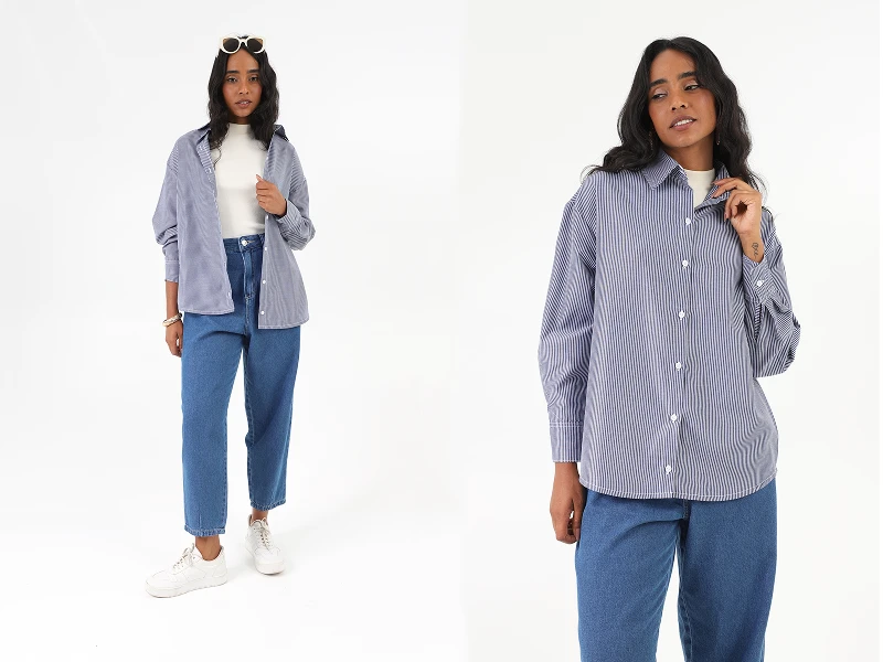 Mulher com camisa às riscas azuis e brancas, calças de ganga e sapatilhas. Visual casual e moderno.