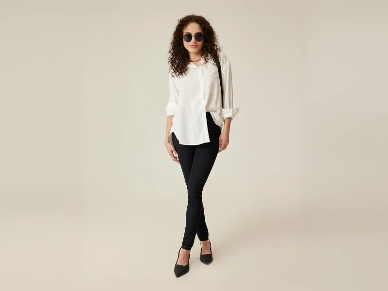 Mulher de camisa branca, calças pretas e sapatos de salto alto. Estilo moderno com óculos de sol e cabelo encaracolado.