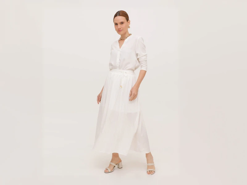 Conjunto feminino branco composto por camisa, saia comprida fluida e sandálias de salto alto.