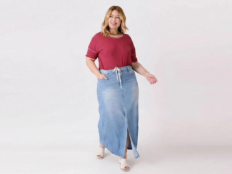 Mulher com t-shirt bordô e saia de ganga maxi com racha frontal e cordão na cintura.