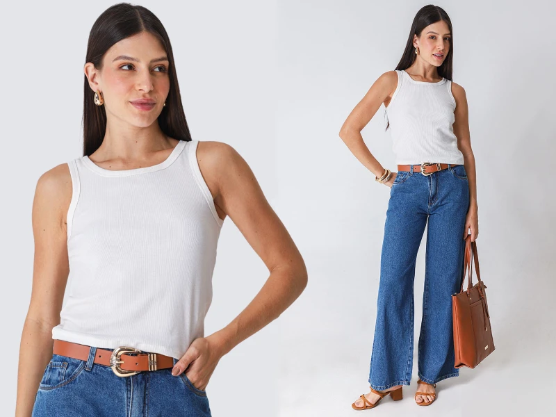 Mulher com top branco canelado, calças de ganga largas e cinto castanho. Visual casual com mala e sandálias.