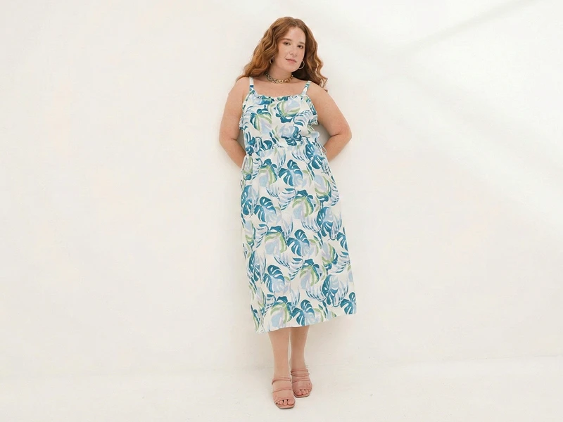 Mulher ruiva com vestido midi branco e padrão tropical em tons de azul e verde sobre fundo branco.