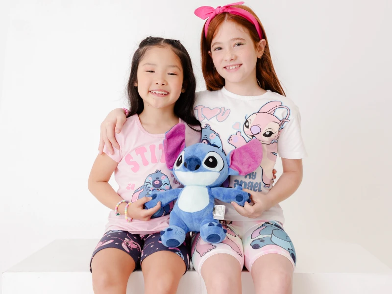 Duas meninas a sorrir com peluche do Stitch e pijamas temáticos Disney Stitch e Angel.