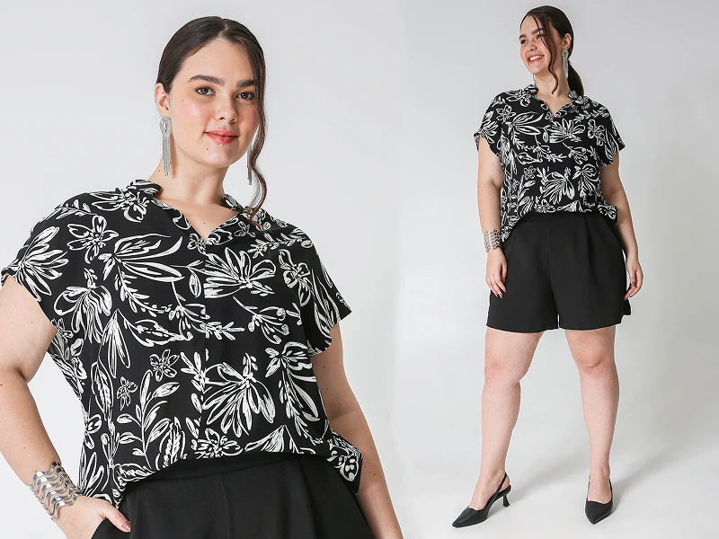Mulher plus size com blusa floral preta e branca, calções pretos e sapatos de salto. Moda feminina elegante.