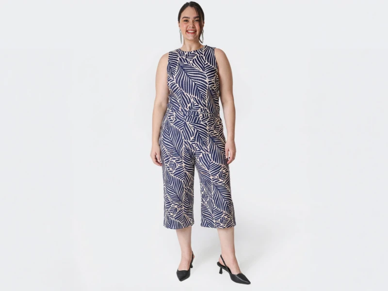 Mulher com macacão sem mangas azul e branco, padrão de folhas e sapatos de salto pretos.