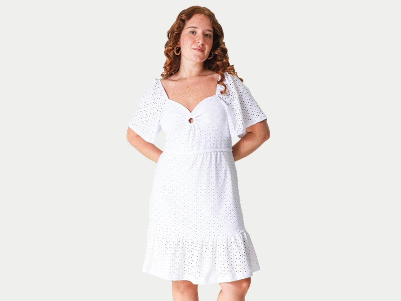 Mulher ruiva com vestido branco curto em bordado inglês, com mangas de folhos e decote em coração.
