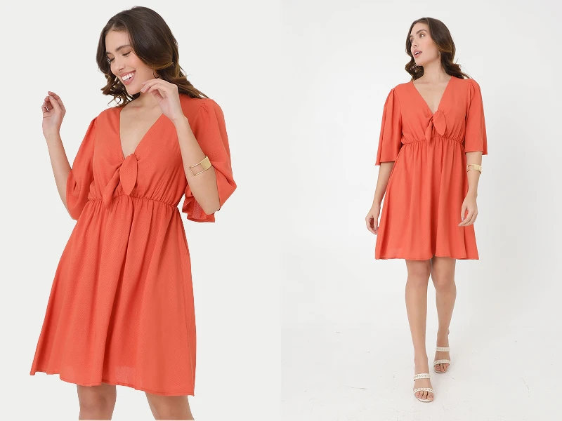 Mulher com vestido curto cor de laranja, decote em V, pormenor de nó e mangas fluidas sobre fundo branco.