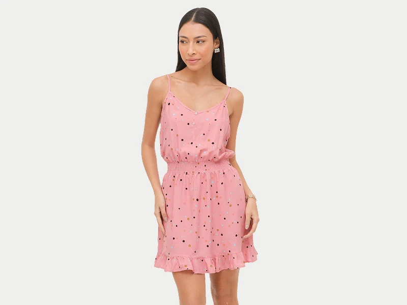 Mulher com vestido rosa curto de alças, padrão de pintas coloridas e folho na bainha.