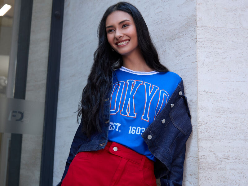 Modelo com blusa azul e saia vermelha em cenário urbano