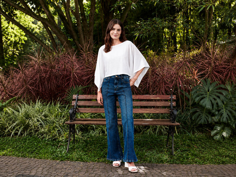 Mulher em outfit casual em parque com bancos e plantas.